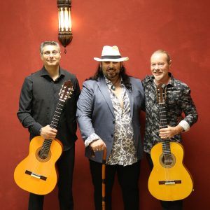 Die drei Bandmitglieder mit zwei Gitarren vor einer roten Wand.